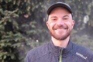 Porträt von Lukas Huber mit dunkelgrünen zweigen im Hintergrund.